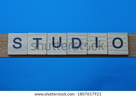 gray word studio in small square wooden letters with black font on a blue background