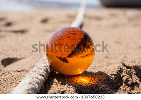 Orange glass ball on sand near the sea. Abstract conceptual photo.