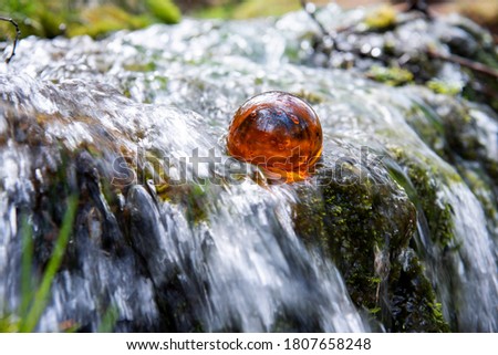 Orange glass ball in small waterfall. Abstract photo of time.