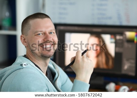 Smiling man holding an electronic pen in his hand from behind on computer background. Learning professions for remote work concept Royalty-Free Stock Photo #1807672042