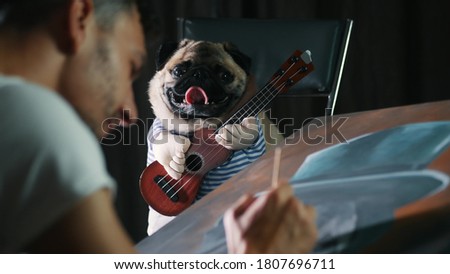 Adorable pug dog posing for the artist in a suit with a guitar, a man painting a picture of a dog in close-up
