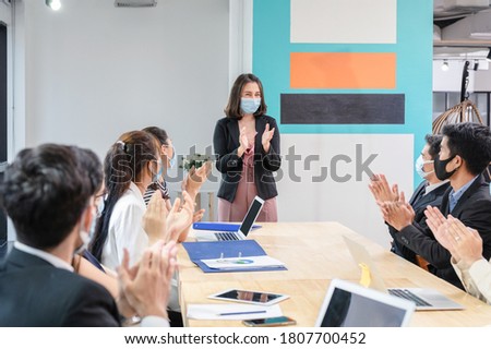 Multi ethnic colleagues celebrating with applauding the female executive while meeting in new normal office. Business team wearing face mask while pandemic of Coronavirus, Covid-19 Royalty-Free Stock Photo #1807700452