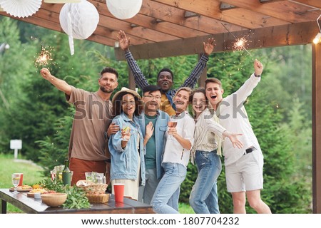 Multi-ethnic group of happy friends holding sparklers and looking at camera while enjoying Summer party outdoors, copy space Royalty-Free Stock Photo #1807704232