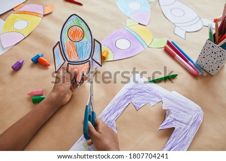 Close up of unrecognizable African-American boy cutting picture of space rocket while enjoying art and craft class in school or children development center, copy space