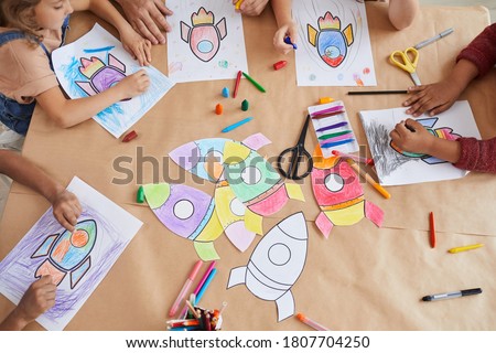 Top view close up at multi-ethnic group of kids drawing pictures of space rockets with crayons while enjoying art and craft class in pre school or development center, copy space