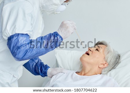Professional doctor wearing protective uniform taking senior woman's swab for dangerous virus test using stick, copy space