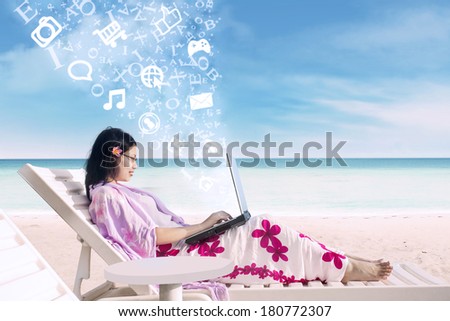 Attractive Asian female surfing online using laptop with flying alphabet at the beach