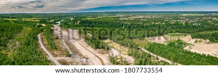 Panorama drone photo on construction of new highway and bridge over Umea river - many heavy industrial machines work together - dump trucks, bulldozer and excavator. Construction site and Umea city