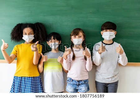 Diversity of children students wearing medical masks in the classroom. Students stand in a row in front of the blackboard with thumbs up.  Prevention of the coronavirus outbreak And new normal Concept Royalty-Free Stock Photo #1807756189