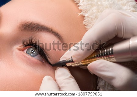 Permanent eye makeup close up shot. Cosmetologist applying tattooing of eyes. Makeup eyeliner procedure Royalty-Free Stock Photo #1807759051