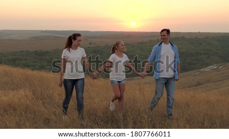 healthy smiling family holding hands walking in field at sunset in mountains, daughter holding mom and dad by hands. happy child and parents walk in rays of beautiful sun, travel on vacation. family