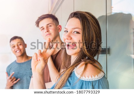 Cool friends pose for a photo.  An attractive woman makes the sign of peace.  She sticks out her tongue and her friends smile.  The focus is on the woman.