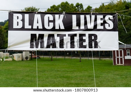 large black and white banner saying Black Lives Matter tied in place in a park area