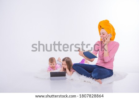 woman with book in her hands is talking on phone. Children watch cartoon on their tablet. mom washed her hair. towel on head. Hobbies and recreation with gadgets.