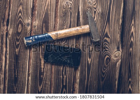 Old big hammer and broken smartphone on a wooden background. Studio photo.