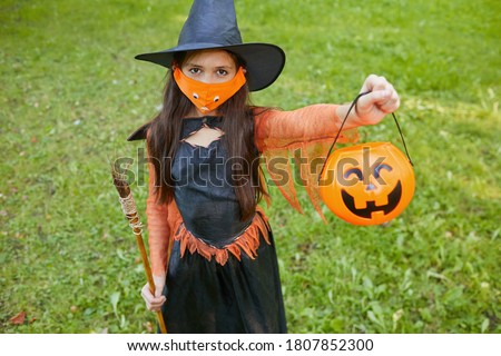 Portrait of little girl in witch costume holding basket and asking for treats while standing outdoors