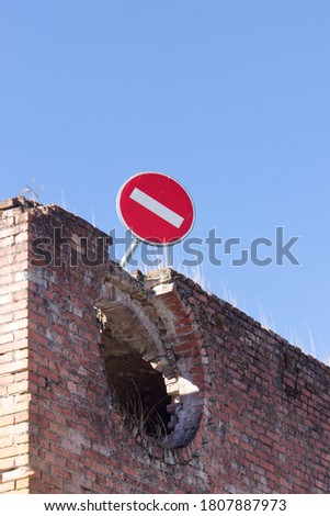 A no entry sign at the top of a brick structure with a bright blue sky in the background.