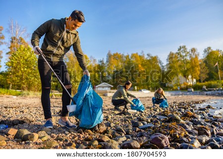 Man cleaning beach with volunteers on sunny day Royalty-Free Stock Photo #1807904593