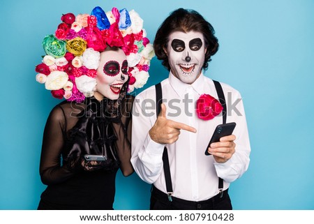 Photo of lovely spooky couple man lady hold direct finger telephone find undead friend social network wear black dress death costume roses headband suspenders isolated blue color background
