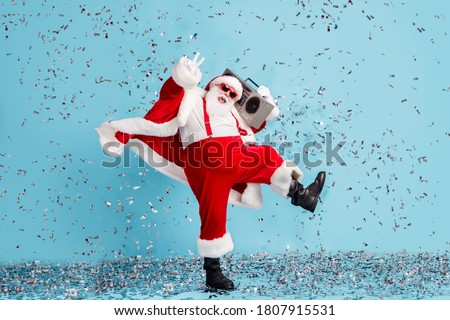 Full length photo of pensioner grandfather funky dance show v-sign confetti hold retro radio wear santa x-mas costume suspender sunglass boot pants cap isolated blue color background
