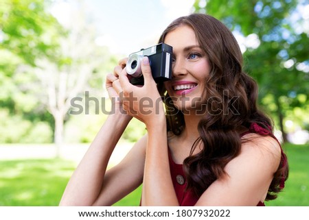 photography, leisure and people concept - happy smiling woman with film camera photographing at summer park