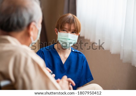 Attractive young Asian female nurse kneeling beside senior patient in wheelchair talking, smiling and cheering up in comfort at hospital. Healthcare and medicine concept. Royalty-Free Stock Photo #1807950412
