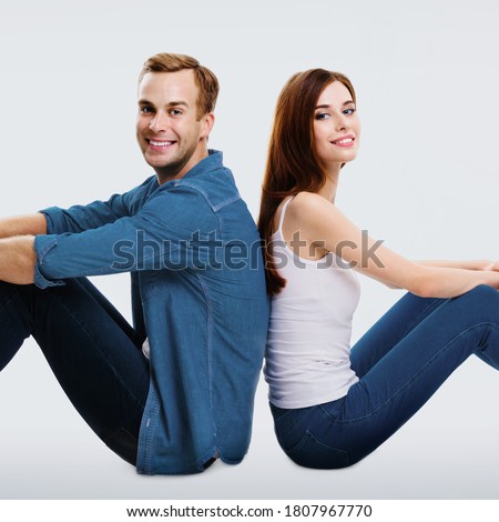 Happy amazed couple. Full body length profile portrait of sitting back to back models in love studio ad concept, isolated over bright grey background. Man and woman together. Square composition image.