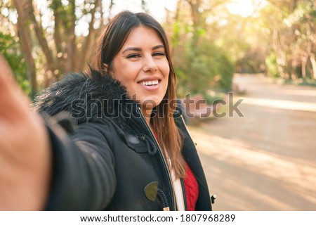 Young beautiful brunette woman smiling happy and confident. Standing with smile on face making selfie by the camera at street of city