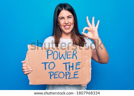 Young woman asking for social movement holding banner with power to the people message doing ok sign with fingers, smiling friendly gesturing excellent symbol