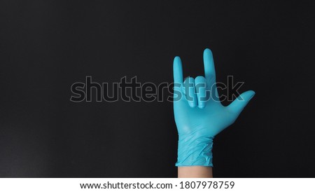 The love-you gesture or I love you hand sign with hand wearing blue glove on black background.