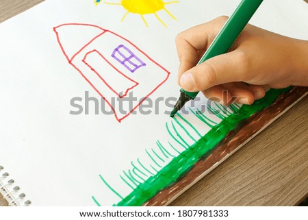 A small child draws a house with markers in the album. Step-by-step instructions.
