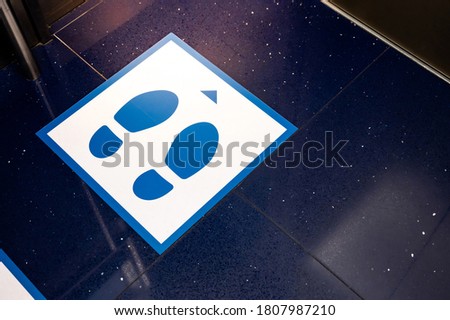 Blue glossy floor of passenger lift or elevator with standing marker for social distancing to avoid spreading coronavirus. Foot symbol position for preventing COVID-19 pandemic in public building.