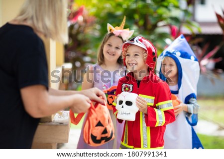 Kids trick or treat in Halloween costume. Children in colorful dress up with candy bucket on suburban street. Little boy and girl trick or treating with pumpkin lantern. Autumn holiday fun.