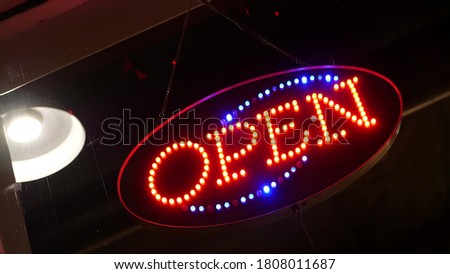 Open neon sign glowing in the dark. Vivid retro styled text at entrance on glass window. Colorful electric banner selective focus close up. Light bulbs radiance at night. Shiny illuminated lettering.