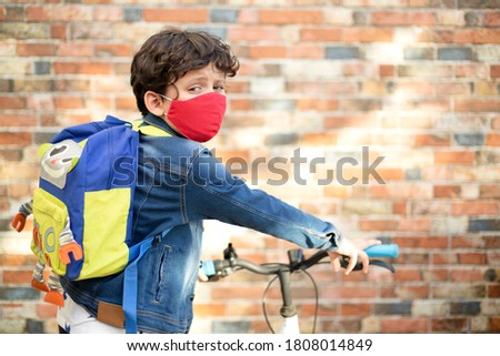 Little boy with a face mask and a backpack riding his bike to school after Covid-19 quarantine. Royalty-Free Stock Photo #1808014849