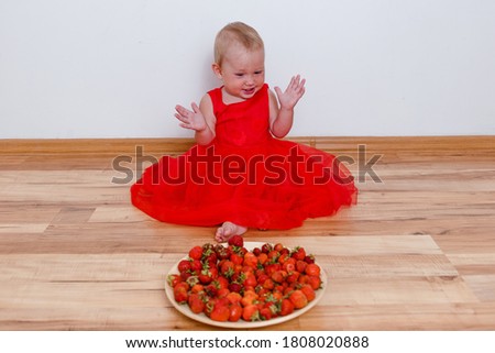 Cheerful girl in red dress slams her hands next to ripe strawberries indoors