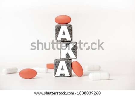 a group of white and red pills and cubes with the word AKA Above the knee amputation. on them, white background. Concept carehealth, treatment, therapy.