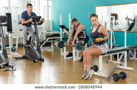 Group of people exercising with weight and on exercise bike in gym
