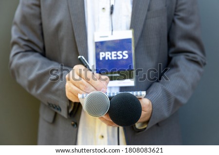 Male journalist at news conference or media event, holding microphone, writing notes. Journalism concept. Royalty-Free Stock Photo #1808083621