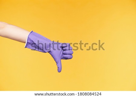 Studio photo of fair-skinned raised hand pointing down with thumb while expressing negative emotions, showing dislike while posing over yellow background