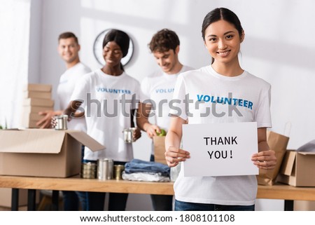 Selective focus of asian woman looking at camera while holding card with thank you lettering in charity center