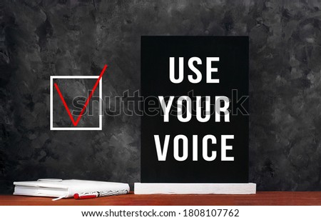 Use Your Voice text sign on black chalkboard with white notebok and red pen on dark background. Message written on blackboard display. Vote elections concept. Make the political choice.