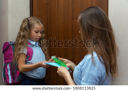 Mom takes her daughter to school and gives her a protective medical mask and antibacterial hand gel (alcohol gel). Back to school. Get your child to school. Social distance and safety