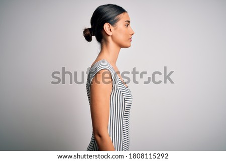 Young beautiful brunette woman wearing casual striped dress over isolated white background looking to side, relax profile pose with natural face with confident smile. Royalty-Free Stock Photo #1808115292