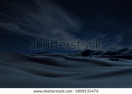 Desert hills and dunes at night under the stars and cloudy sky in blue atmosphere.                  