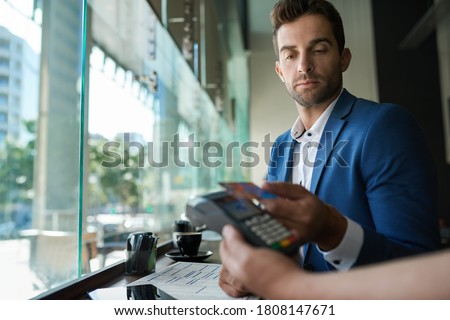 Man sitting at a counter in a cafe and paying his waiter using an nfc terminal and credit card Royalty-Free Stock Photo #1808147671