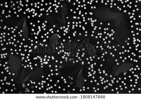 Cartoon Halloween background black bats and silver star shaped confetti on black backdrop. Dark and moody holiday backdrop for your design. Night sky concept. Flat lay style.