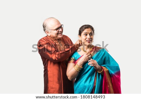 Indian old man tying or presenting gold necklace to his beautiful wife on birthday, valentine day, anniversary or Diwali festival