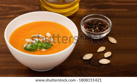 Pumpkin and carrot soup with pumpkin seeds on wooden background.