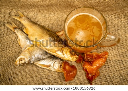 Dried fish, dried caviar and a beer mug on a homespun cloth with a rough texture. Close up.